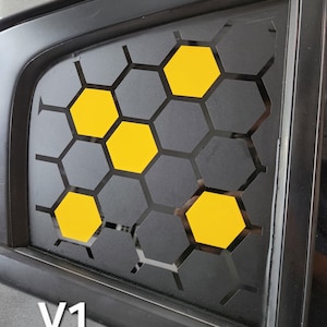 May include: A car window vent cover with a honeycomb design. The cover is black with yellow honeycomb shapes. The text "V1" is in white at the bottom left corner of the window.