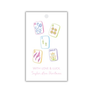 Puede incluir: Una etiqueta de regalo blanca con una ilustración colorida de cinco cartas de juego. Las cartas son un número 2, un número 3, un número 4, un comodín y una carta con un diseño de espiral. El texto "WITH LOVE & LUCK" y "Taylor Ann Hartman" está impreso en la etiqueta.