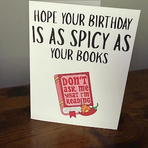 May include: A white birthday card with the text "HOPE YOUR BIRTHDAY IS AS SPICY AS YOUR BOOKS." The card features an illustration of a book with a chili pepper and the text "DON'T ask me what I'm READING."