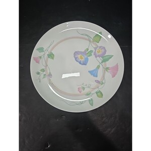 Op de afbeelding: Witte keramische plaat met een bloemenontwerp met winde in blauwe, paarse en roze tinten. De bloemen zijn omgeven door groene bladeren en een delicate roze en perzik ring.