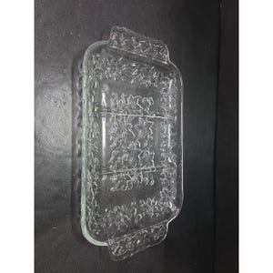 Puede incluir: Fuente de servir de vidrio transparente con forma rectangular y estampado floral. El plato tiene tres compartimentos y asas en cada extremo. El diseño floral está en relieve sobre el vidrio.