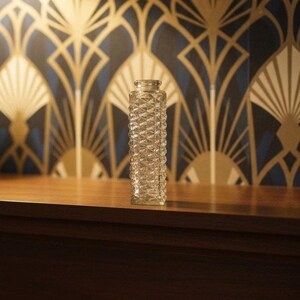 May include: A clear glass bud vase with a square base and a tall, slender body featuring a textured, geometric diamond-cut pattern throughout its exterior surface, topped with a small, circular opening at the narrow neck of the vessel.