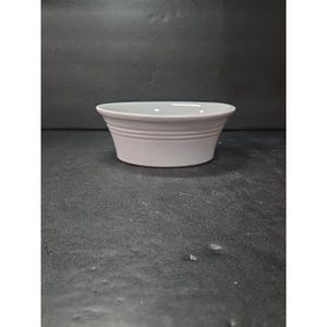 Puede incluir: Un cuenco de cerámica de color lila claro, con un diseño ancho y poco profundo. El cuenco tiene un acabado liso y brillante y una forma sencilla y elegante. El exterior presenta estrías horizontales. Ideal para servir aperitivos o platos pequeños.
