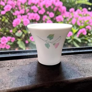 May include: A white ceramic mug with a black handle and the text "But First, Coffee" in a bold, black font. The mug is set against a blurred background, suggesting a cozy setting.