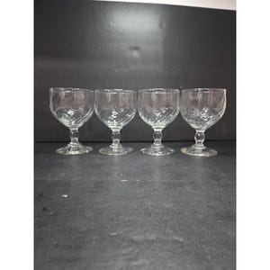 Può includere: Quattro bicchieri trasparenti con un motivo a spirale sulla coppa. I bicchieri hanno una coppa arrotondata e un gambo corto. I bicchieri sono disposti in fila su una superficie scura. I bicchieri sono probabilmente per servire vino o altre bevande.