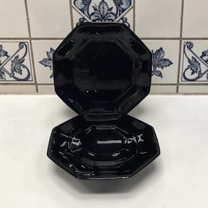 May include: Two black, octagonal serving dishes. The dishes are made of a glossy material and have a geometric design. The top dish is open, revealing the interior. The dishes are stacked on top of each other.