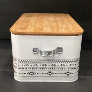 Side view of the white bread box showing a silver metal handle and the patterned border wrapping around.