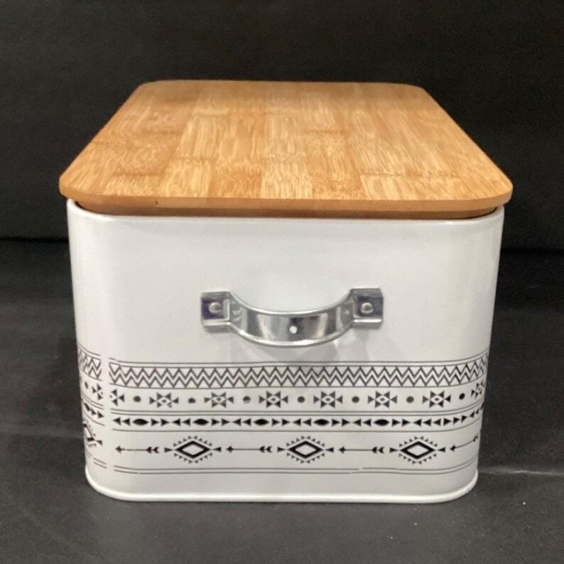 Side view of the white bread box showing a silver metal handle and the patterned border wrapping around.