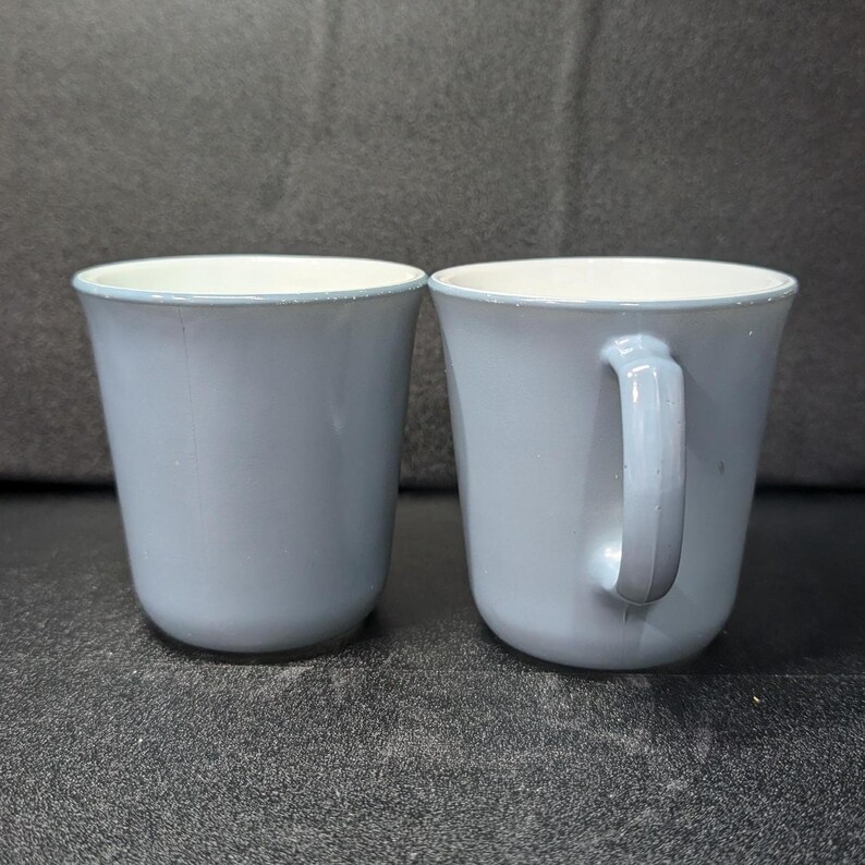 Two light blue coffee mugs positioned side by side, showing one mug viewed from the front and the other from the side with its handle.