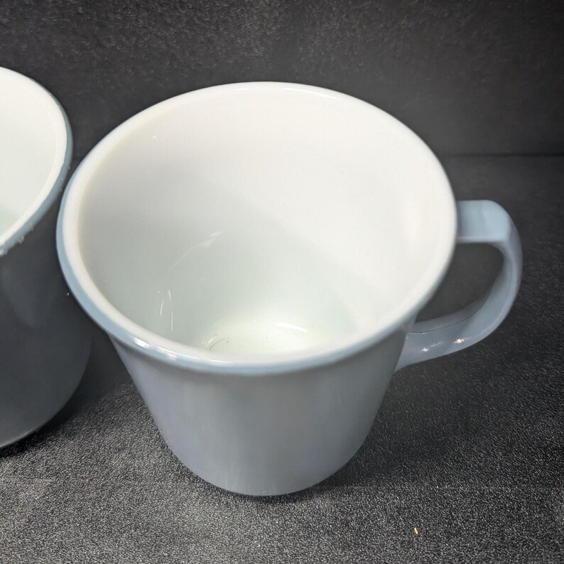 Angle shot of a light blue coffee mug facing forward with its handle on the right side against a dark gray background.