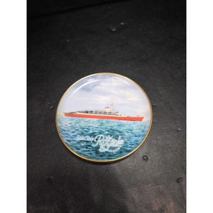 May include: A decorative plate featuring a red and white ship sailing on blue water under a cloudy sky. The plate has a gold rim and the words "Starship Royale" are written in a stylized font.