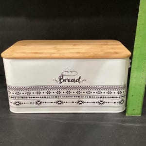 A white bread box with a bamboo lid has a green ruler placed vertically next to it for scale.