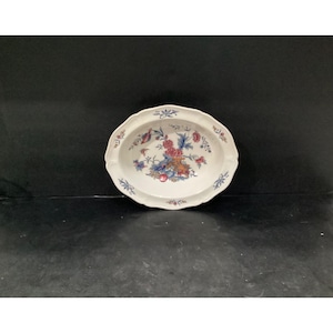 May include: An oval ceramic serving dish with a scalloped edge and a white base. The center features a detailed floral pattern in shades of red, blue, and orange, with additional small floral motifs decorating the rim of the dish.
