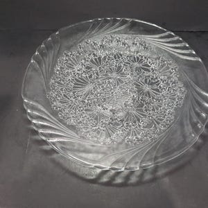May include: A clear glass serving platter with a raised floral design. The design features a repeating pattern of small flowers.