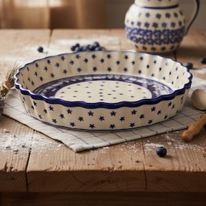 May include: A round ceramic quiche dish with a scalloped edge, featuring a cream-colored base decorated with a repeating pattern of small blue stars and a blue rim. The interior base displays a central star pattern surrounded by a blue circular border.