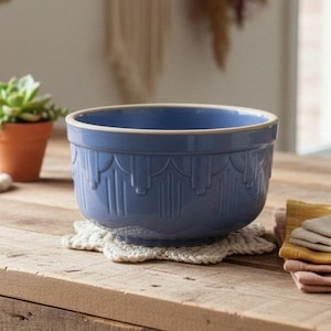 May include: A medium-sized, round ceramic mixing bowl in a solid periwinkle blue colour. The exterior features a repeating embossed arch and vertical line pattern around the circumference. The rim is smooth and finished in a light cream tone.