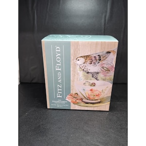 May include: A box for a tea set with the words "Fitz and Floyd" in white. The box features a bird and floral design with the words "The English Garden Collection" and "Tea Cup, Saucer & Tea Rest Set of 3".