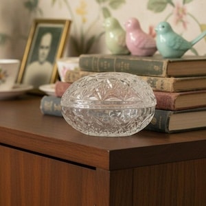 May include: A clear, oval-shaped glass trinket box featuring a faceted, diamond-cut pattern across its surface. The container consists of a base and a matching removable lid, both crafted from transparent glass with a reflective, textured finish.