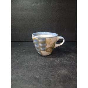 May include: A ceramic teacup with a blue rim and handle. The cup is decorated with blue and tan floral patterns. The cup is filled with a white liquid. The cup is on a dark surface.