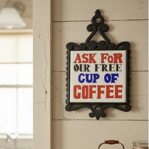 May include: A square white ceramic tile sign set in a black decorative cast iron frame with a hanging loop. The tile features the text ASK FOR OUR FREE CUP OF COFFEE in red, black, and blue lettering. The sign is designed for wall mounting.