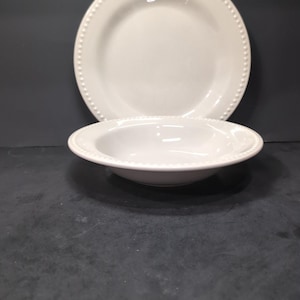May include: A white ceramic bowl and a white ceramic dinner plate with a beaded rim.