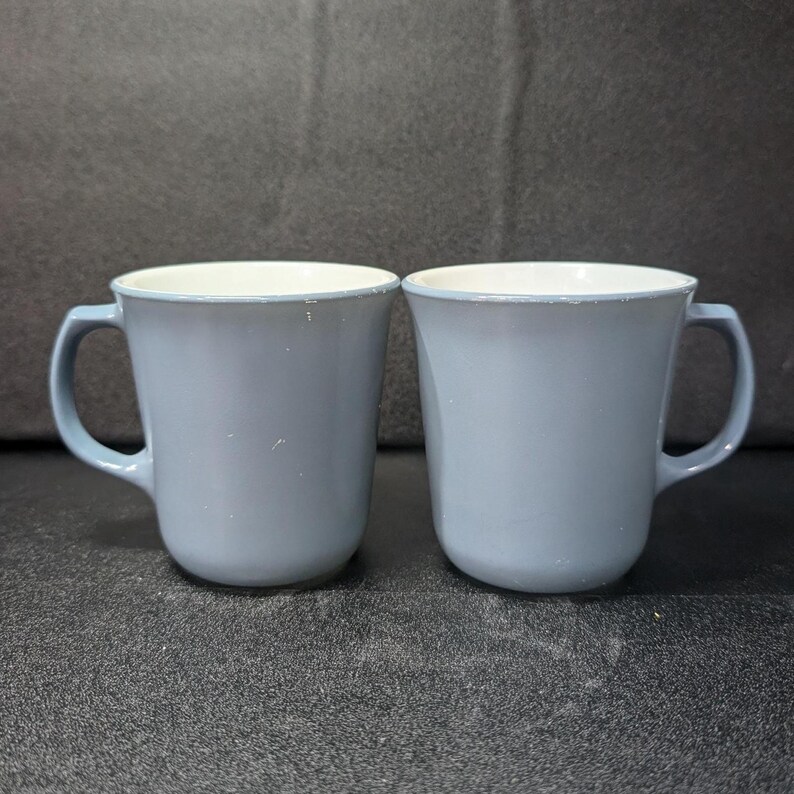 Front view of two light blue coffee mugs standing side by side with handles facing outward.