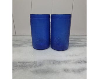 Può includere: Due bicchieri blu cobalto con superficie strutturata. I bicchieri cilindrici hanno un design semplice e classico. I bicchieri sono realizzati in un materiale solido e opaco.