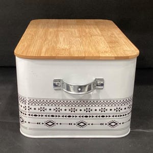 A rectangular white metal bread box with a wooden lid, silver metal side handle, and a black geometric pattern around the lower half.