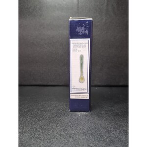 May include: A tall, navy blue box featuring a porcelain spoon. The box has text that reads "SPRING FREESIA FLOWER DESIGN PORCELAIN SCULPTURED SPOON". The spoon is green and yellow with a flower design on the bowl.