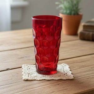 May include: A tall, cylindrical drinking glass in a vibrant, translucent red hue. The exterior surface features a repeating, raised circular pattern that creates a textured, dimpled effect across the entire body of the glass vessel.