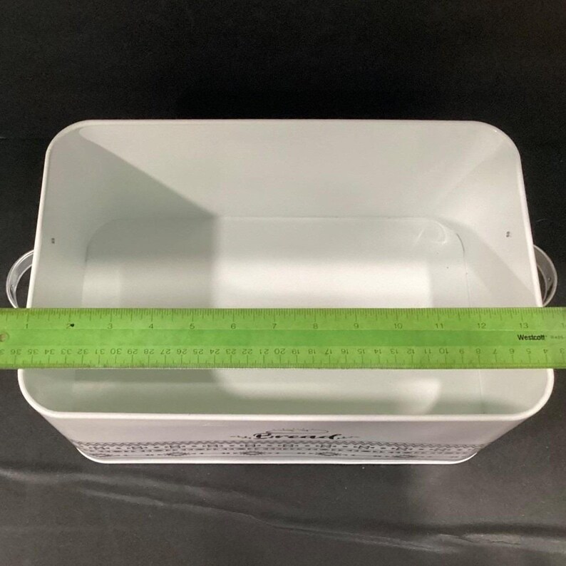 An open white bread box with metal handles viewed from above, measured with a green ruler across the interior.