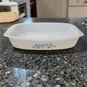 May include: A rectangular, off-white baking dish with rounded corners. The dish features a delicate blue floral pattern along the bottom edge. The dish is made of a durable material, perfect for oven use.