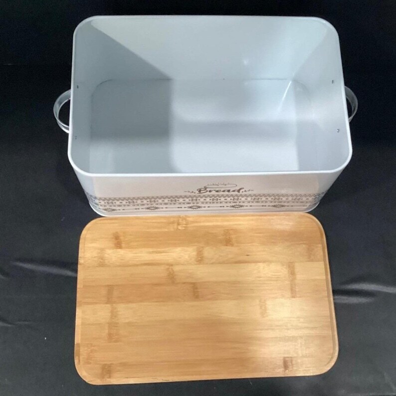 The white bread box is shown with its bamboo lid removed and placed flat in front of it.