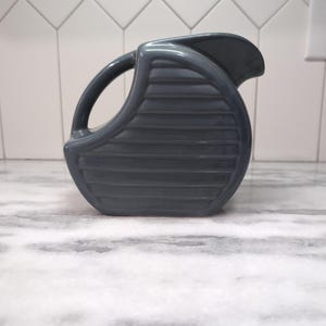 May include: A gray ceramic pitcher with a ribbed design. The pitcher has a rounded shape and a handle.