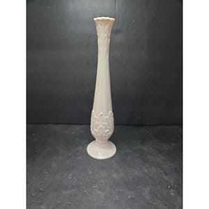 May include: A tall, off-white ceramic vase with a fluted design. The vase has a flared top and a decorative floral pattern near the base. The vase stands approximately 12 inches tall.