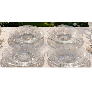 May include: A set of four clear glass bowls featuring an embossed pattern of grape clusters and vine leaves. Each bowl has a wide, shallow basin and a textured rim, showcasing a detailed botanical design pressed into the transparent glass surface.