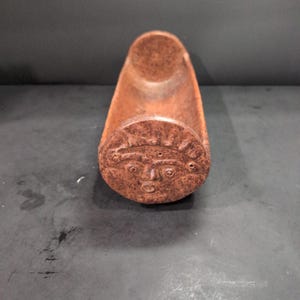 May include: A brown ceramic incense holder shaped like a long, narrow boat with a carved face on one end.