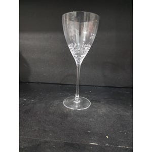 May include: A clear, stemmed wine glass with a wide bowl and a delicate, patterned design near the base. The glass has a long, slender stem and a circular base. The glass is made of clear glass.