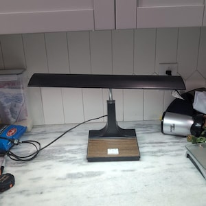 May include: A black and brown desk lamp with a long, flat shade. The lamp is on a white countertop.