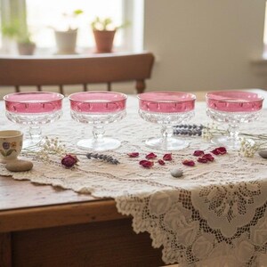 Può includere: Quattro coppe da dessert in vetro trasparente con un ampio bordo rosa vivace e una base sfaccettata e testurizzata. Ogni coppa poggia su uno stelo corto e robusto. Il design presenta un delicato dettaglio a perline lungo la transizione tra il bordo rosa e il corpo in vetro trasparente, creando un aspetto raffinato e classico per servire dolci.