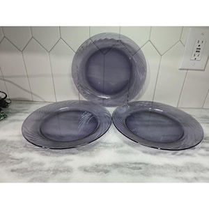 Może przedstawiać: Trzy owalne, fioletowe talerze ze szkła z spiralnym wzorem na krawędziach. Talerze ułożone są na jasnej powierzchni, z jednym talerzem pośrodku i dwoma innymi ustawionymi pod kątem do boków. Talerze są puste.