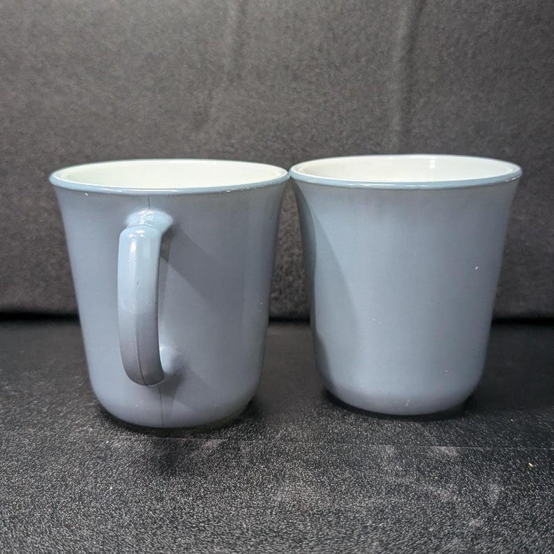 Two light blue coffee mugs placed next to each other, with the left mug showing its handle profile and the right mug facing forward.