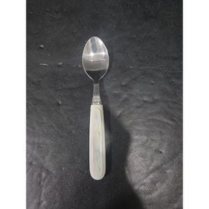 Puede incluir: Una cuchara de acero inoxidable con un mango blanco con un diseño floral en azul y verde. La cuchara tiene un cuenco clásico de forma ovalada y un mango decorativo, adecuado para servir o comer.