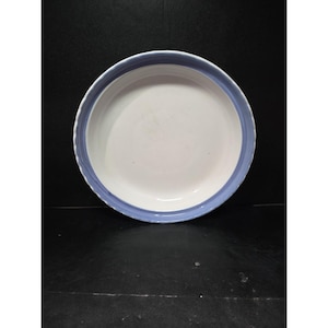 Puede incluir: Un plato redondo de cerámica blanca con un borde azul claro. El plato tiene un borde ligeramente elevado y un acabado liso y brillante. El borde azul es de color sólido y añade un toque de color al plato blanco.