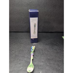 Op de afbeelding: Een decoratieve lepel met een groen, wit en blauw ontwerp. De lepel heeft een gedetailleerde handgreep met een bloemen- en vogelmotief. Een blauwe doos met tekst staat op de achtergrond.