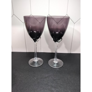 May include: Two elegant wine glasses with a gradient purple bowl and clear stem. The bowl features a geometric design. The stem has a unique, curved design. The glasses are set against a white and black background.