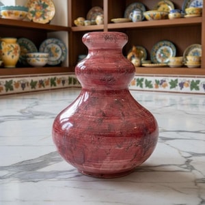 May include: A bulbous, double-gourd shaped ceramic vase with a glossy finish. The vase features a deep red and maroon color palette with horizontal brushstroke textures and subtle dark marbling throughout its rounded, symmetrical body.