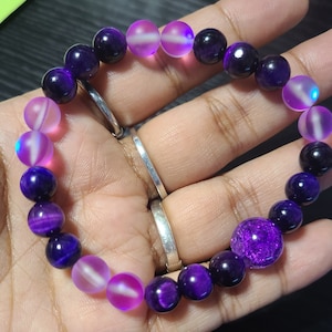 May include: A purple and pink beaded bracelet with iridescent beads. The bracelet is made with tiger's eye and amethyst beads.