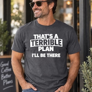 Op de afbeelding: Een antracietgrijs T-shirt met korte mouwen en een ronde hals, voorzien van de witte tekst "THAT'S A TERRIBLE PLAN I'LL BE THERE" op de borst. Het shirt is gemaakt van een zachte, gemêleerde stof en wordt gedragen met een blauwe spijkerbroek.