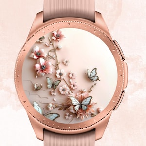 Puede incluir: Un reloj inteligente en oro rosa con una correa rosa claro. La esfera presenta un diseño floral en 3D con flores rosas y mariposas. El texto "Babe in Bloom CREATIONS" está en la parte superior.